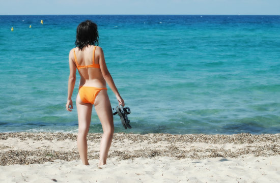 Woman in orange bikini holding flops on the shoreline