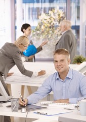 Young designer sitting at desk, colleagues working