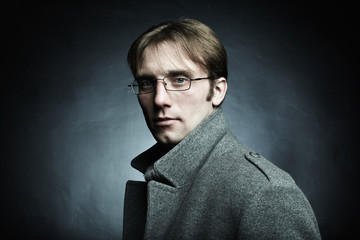 Artistic dark portrait of the young beautiful man in a gray coat