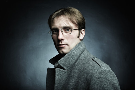 Artistic dark portrait of the young beautiful man in a gray coat