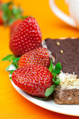 cake on a plate and strawberries lying on the orange fabric