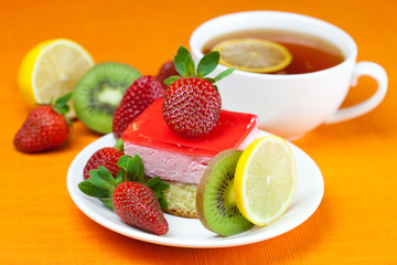 Fototapeta na wymiar lemon tea, kiwi,cake and strawberries lying on the orange fabric