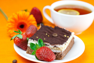 gerbera, lemon tea, cake and strawberries lying on the orange fa