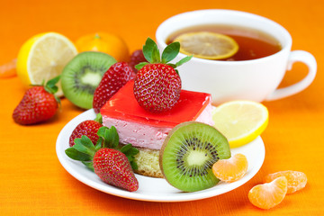lemon tea, kiwi,cake and strawberries lying on the orange fabric