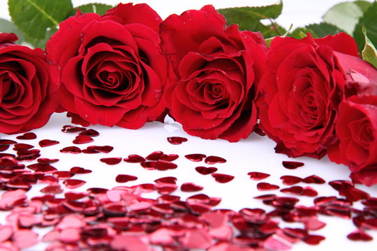 Red roses and heart shaped confetti on white background