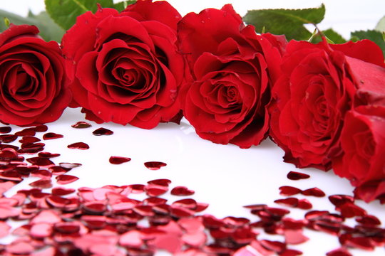 Red roses and heart shaped confetti on white background