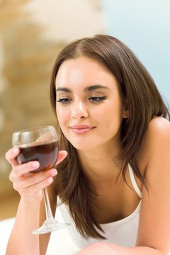 Portrait of young woman with glass of red wine, on bed