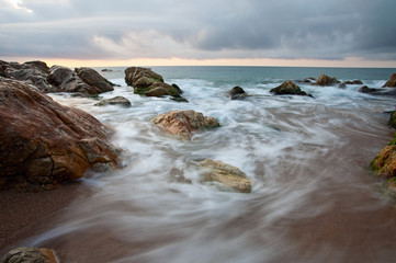 Seascape at sunset with motion blurred waves crashing on rocks