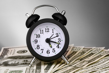 Alarm clock and dollars on gray background