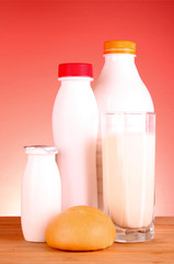 Bottle of milk, loaf and glass on red background