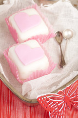 heart shaped pink cupcakes in  tin tray with spoons , red backgr