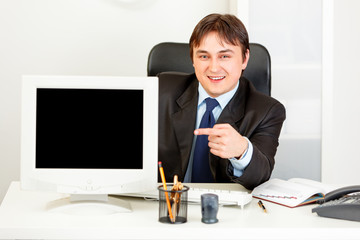 Smiling businessman pointing at  monitor with blank screen.