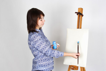 Fototapeta na wymiar young girl in blue shirt standing near easel and painting, blank