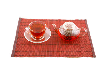 Glass cup of tea and teapot on bamboo placemate isolated