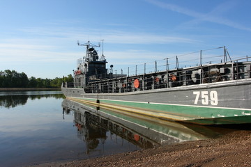 Transport military barge at the river bank against a blue sky