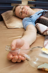 A young man sleeping on the couch with a bottle of wiskey