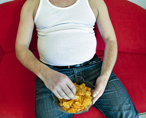 fat man on red couch eating potato chips.