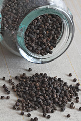 Black pepper corns pouring out oh the glass pot.