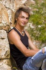 a handsome man is sitting in a shabby jeans between the ruins