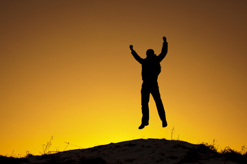 Szczęśliwy mężczyzna skacze na szczycie góry o zachodzie słońca