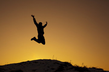 Szczęśliwy mężczyzna skacze na szczycie góry o zachodzie słońca