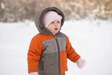 Fototapeta na wymiar Adorable baby stay on snowy road in park and look to tree side