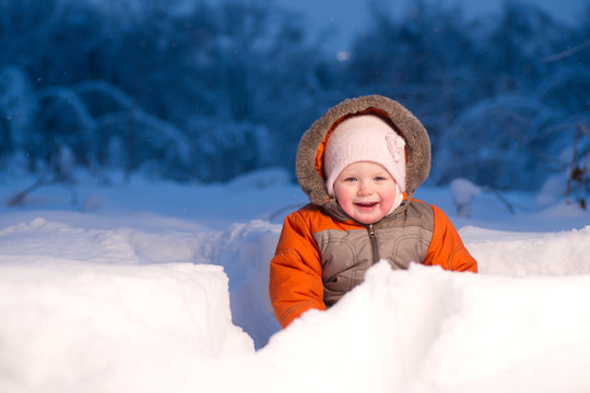 Adorable baby sit and digging hideout hole in snow in field in t