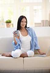 Pretty woman on sofa having tea using computer