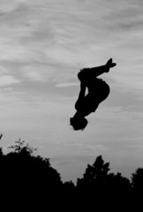 silhouette of gymnast on trampoline in sky doing back somersault