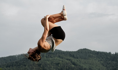 female gymnast doing back somersault in nature - obrazy, fototapety, plakaty