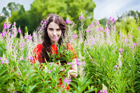 Smiling girl in red dress looking through the flowers on the mea