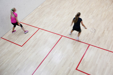 Two female squash players in fast action on a squash court (moti