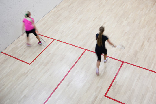 Two female squash players in fast action on a squash court (moti