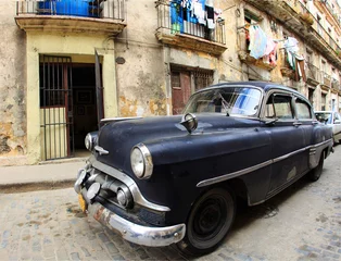 Selbstklebende Fototapeten Ein klassisches altes Auto ist schwarz vor dem Gebäude geparkt © maxoidos