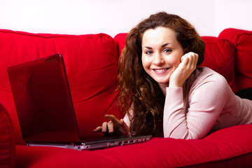 junge Frau mit Laptop auf Sofa liegend