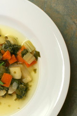 Partial view of a  white bowl of kale and vegetable soup