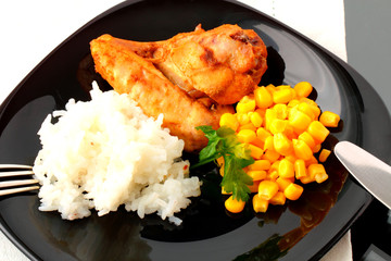 A piece of roast chicken with rice and corn on the black plate