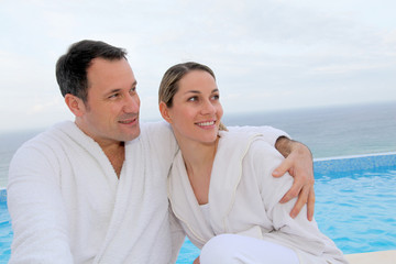Obraz premium Couple in bathrobe sitting by swimming-pool