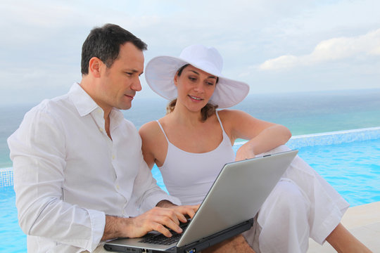 Couple using laptop computer by swimming-pool