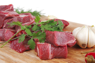 beef meat chunks on wooden cutting plate with hot red peppers