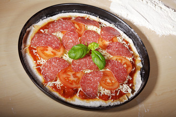 Salami Pizza roh im Backblech und Mehl