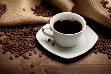 Fototapeta premium Cup of coffee and beans on jute background