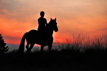 Fotobehang Paardrijden Een ruitersilhouet te paard bij zonsondergang