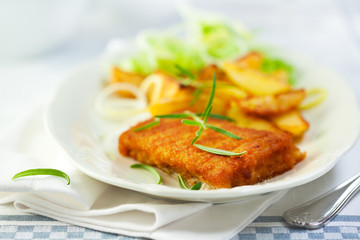 Breaded fish fillet with baked potatoes and herbs
