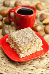 cake on a plate, nuts and a cup of coffee on a wicker mat