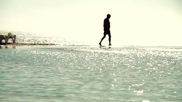 A dark silhouette image of man walking along a beach