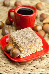 cake on a plate, nuts and a cup of coffee on a wicker mat