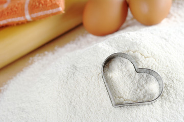 Heart shaped cookie cutter on flour with eggs