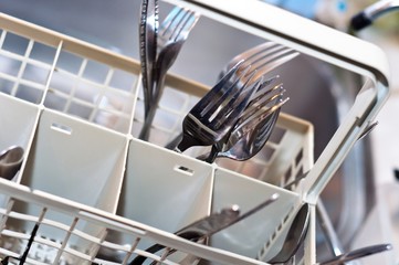 Forks and knives in washing machine with blurry background