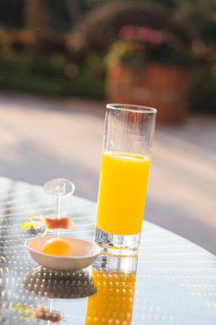 Glass of orange juice and ice cream on table in a garden.